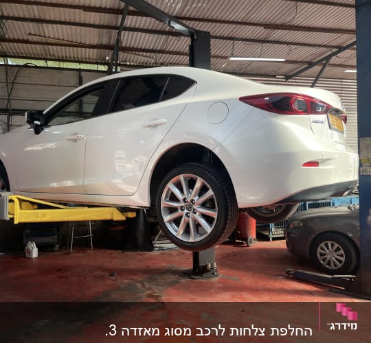 רכב לבן מורם על ליפט במוסך